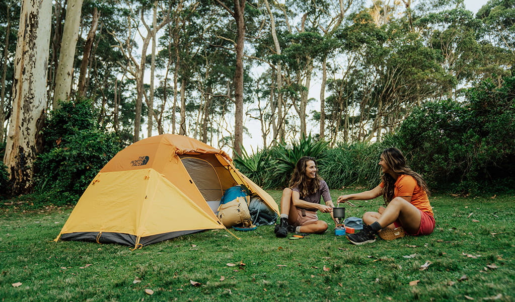 2 campers cooking in front of a tent surrounded by trees in Murramarang National Park. Credit: Remy Brand &copy; DPE