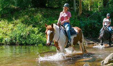 A pair of women on horseback make a river crossing.  Photo credit: Andrew Cooney &copy; Glenworth Valley Outdoor Adventures