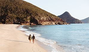 A couple walking along the beach at Tomaree National Park. Photo: Tim Clark/DPIE