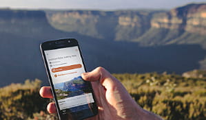 Hand holding a phone with NSW National Parks app on screen. Photo: Branden Bodman/DPIE