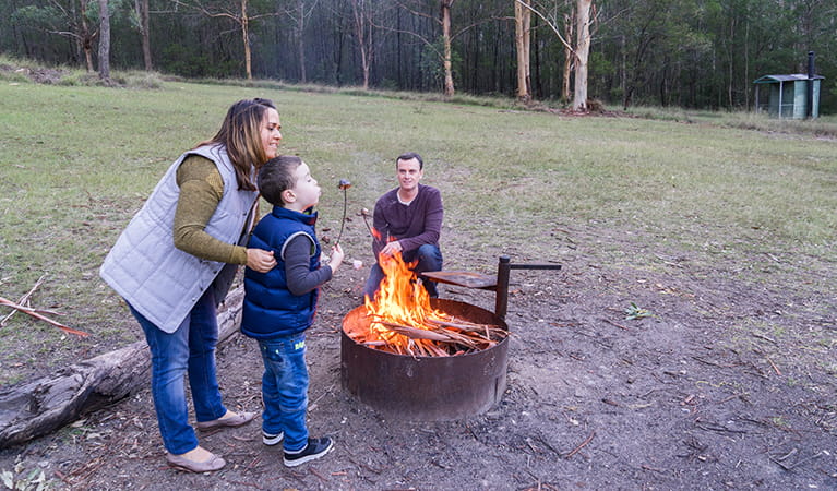 Family roast marshmellows by a fire in the Nikoa section of Euroka campground. Photo: OEH/Simone Cottrell