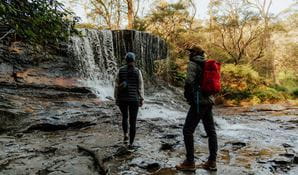 2 walkers on Grand Cliff Top Walk admiring the waterfall at Weeping Rock, Greater Blue Mountains Heritage Area. Photo: Remy Brand &copy; Remy Brand