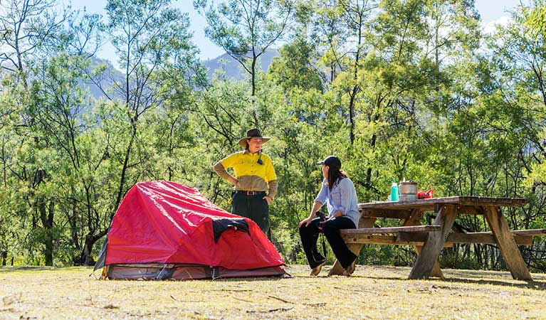 A camper and a ranger sit at a picnic table beside a tent, Kedumba River Crossing campground, Blue Mountains National Park. Photo: Simone Cottrell/OEH