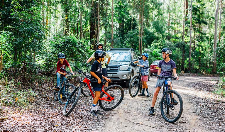 A man and 4 children with mountain bikes stand next to vehicles on one of the Muurlay Baamgala cycle trails. Photo: Jay Black/DPIE