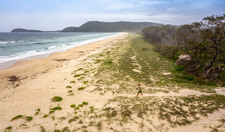 Aerial view of man crossing Seven Mile Beach with a distant headland in the background. Photo credit: John Spencer &copy; DPIE