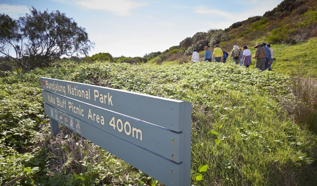 A group of people walking towards Iluka Bluff picnic area, past park signage in Bundjalung National Park. Photo: Nick Cubbin &copy; OEH 