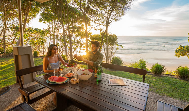 Couple eating outdoors at sunset with views of the beach from Mildenhall Cottage. Photo: John Spencer &copy; DPIE