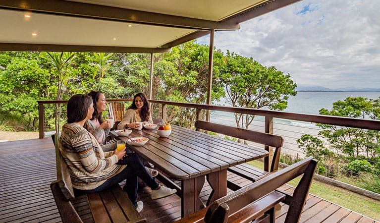 Friends having breakfast with ocean views on the verandah of Thomson Cottage. Photo: Sera Wright &copy; DPIE