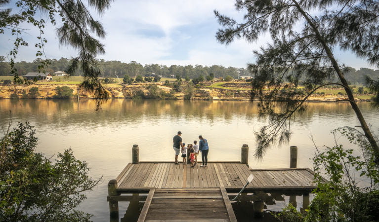 A family standing on a wooden jetty, looking across the Hawkesbury River, at Cattai Farm picnic area in Cattai National Park. Photo: John Spencer/OEH