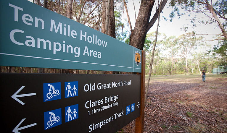 A visitor enters Ten Mile Hollow campground behind a sign for the campground in Dharug National Park. Photo: Nick Cubbin/DPIE