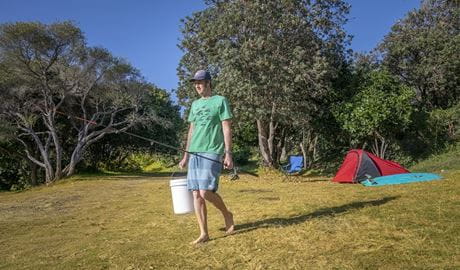 Camper with his fishing rod and bucket heading to the nearby beach, Goolawah National Park. Photo: John Spencer/OEH