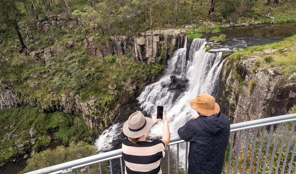 Visitors at Ebor Falls lookout in Guy Fawkes River National Park taking a photo of the falls with their phone. Photo: David Waugh, &copy; DCCEEW