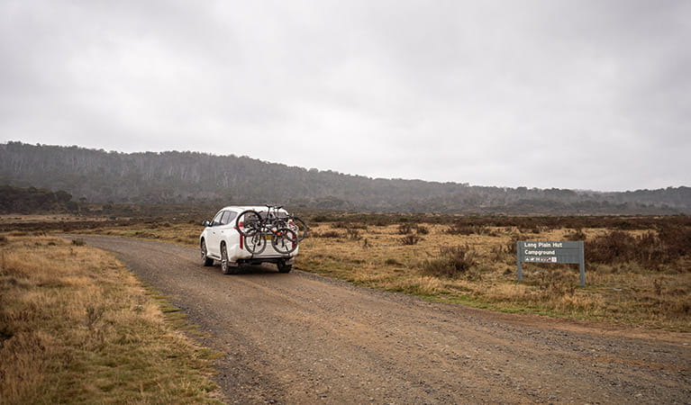 A car carrying bikes drives past a sign on an unsealed road, Kosciuszko National Park. Photo: Robert Mulally/OEH
