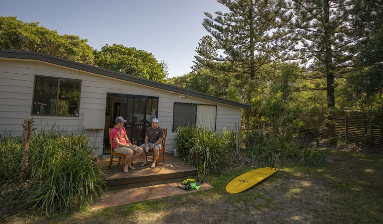 2 people sitting outside on the deck drinking a cup of coffee at Plomer Beach House, Limeburners Creek National Park. Photo: John Spencer/OEH
