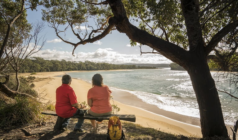 2 people sitting on a bench seat looking out the Bithry Inlet, mouth of the Wapengo Lake in Mimosa Rocks National Park. Photo: John Spencer/OEH