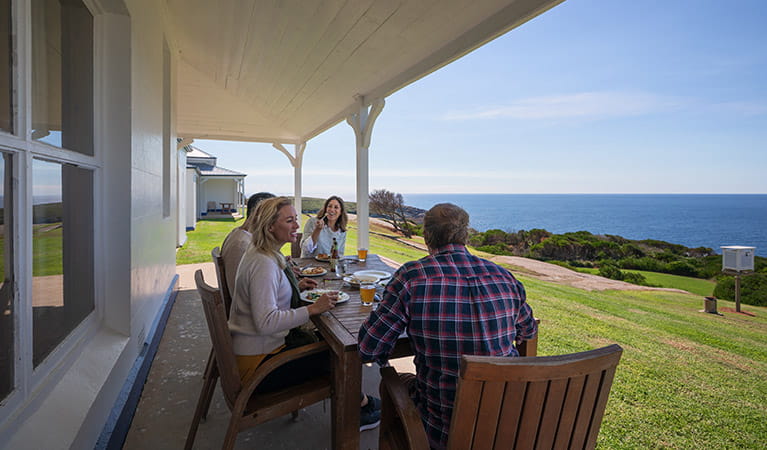 2 men and 2 women lunch at a table on the verandah outside Montague Island Head Lighthouse Keepers Cottage. Photo: Daniel Tran/OEH