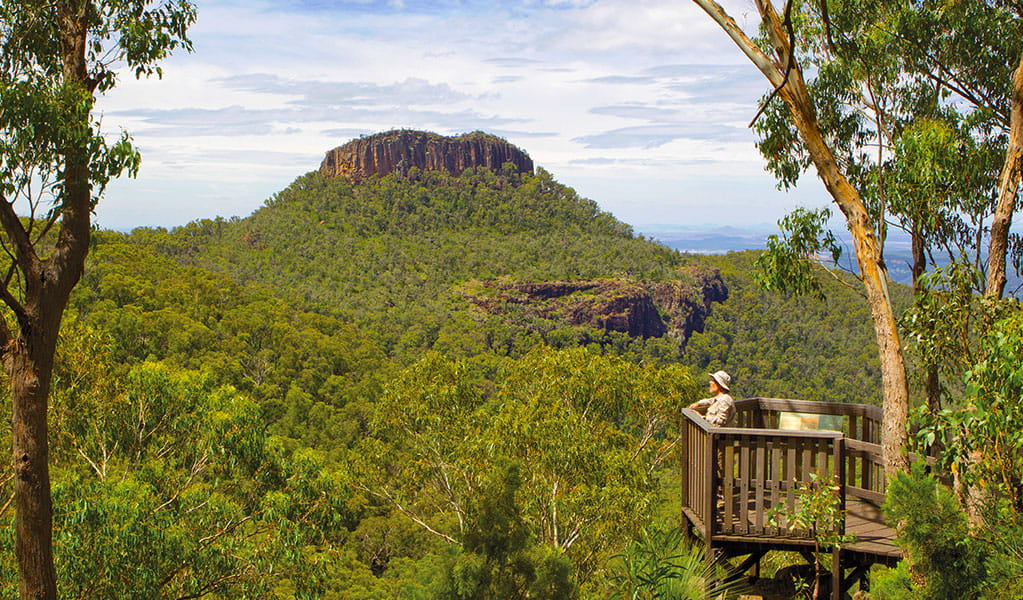 A visitor stands on the wood viewing platform of Euglah Rock lookout, overlooking a valley and Euglah Rock. Photo &copy; Robert Cleary