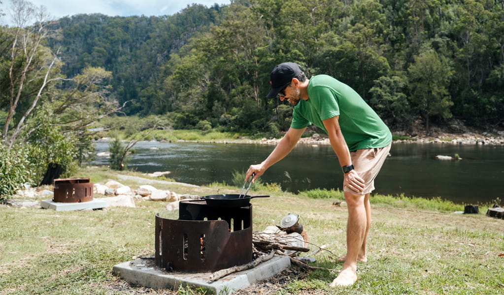 Person cooking on a fire pit at The Junction campground by Nymboida River, Nymboi-Binderay National Park. Photo: Jay Black, &copy; DCCEEW