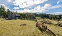 Alexanders Hut with old farm machinery in foreground and forest in background. Photo credit: John Spencer &copy; DPIE