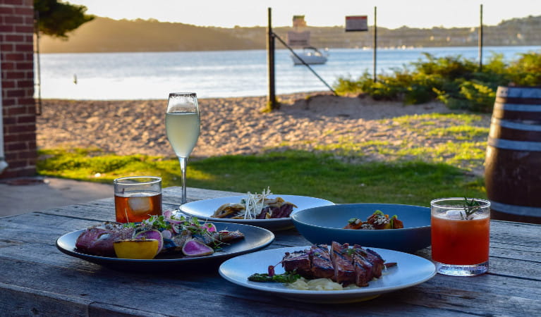 Food and drinks on a table with Sydney Harbour in the background. Photo: Q Station