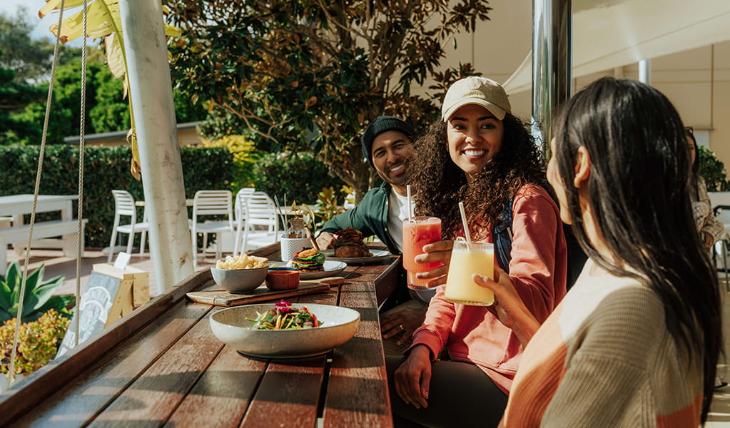 Three hikers having an al fresco lunch at a cafe in Fingal Bay with salads and drinks. Credit: Remy Brand &copy; Remy Brand