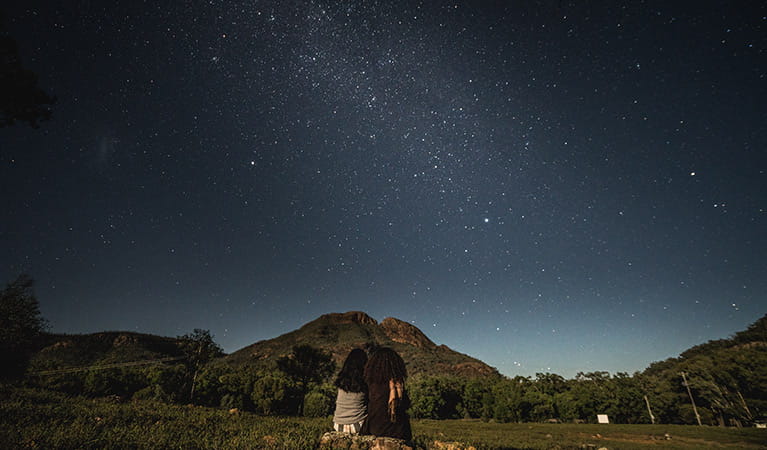 Two women sit side-by-side, stargazing in Warrumbungle National Park. Photo: Robert Mulally/OEH