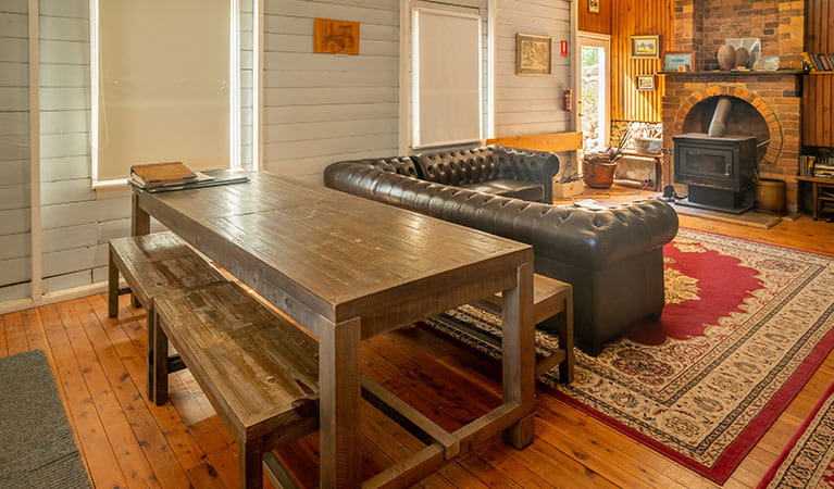 A long wooden dining table, sofa and wood heater at Post Office Lodge in Yerranderie Regional Park. Photo: John Spencer/OEH