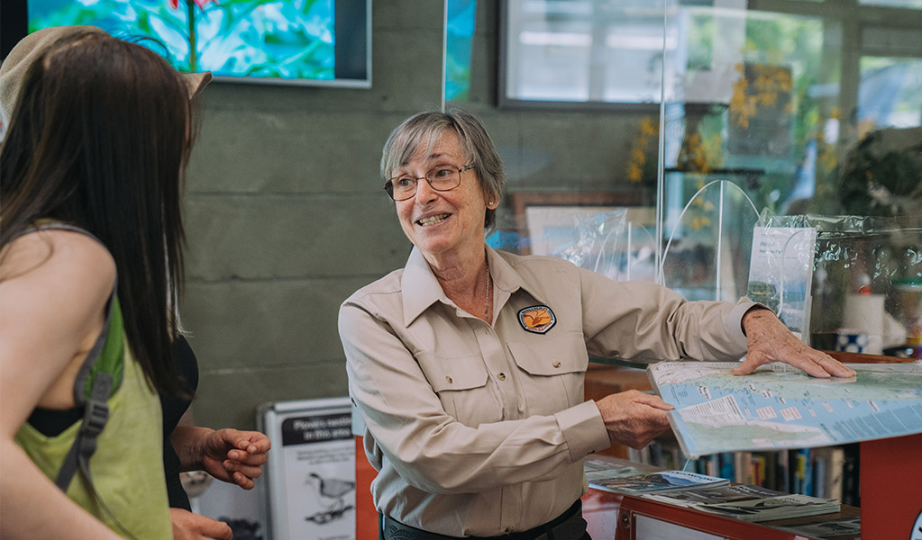 An NPWS staff member showing a visitor a map at a visitor's centre. Credit: Remy Brand &copy; DPE