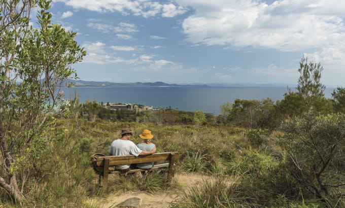 A couple rest on a picnic bench with an ocean view on Monument track. Photo credit: David Finnegan &copy; DPIE