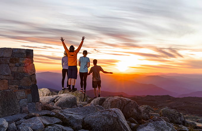 A group of 4 people stand near a rock cairn at the summit of Mount Kosciuszko at sunset. Photo &copy; Thredbo Resort