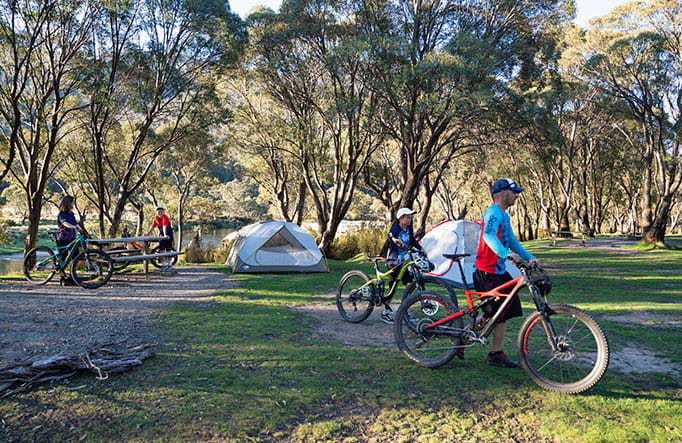 A family walk their mountain bikes past tents at Thredbo Diggings campground in Kosicuszko National Park. Photo: Robert Mulally/OEH
