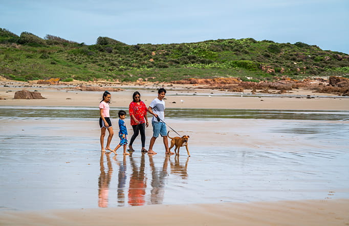 A family walks a leashed dog on a beach. Photo: John Spencer &copy; DPIE
