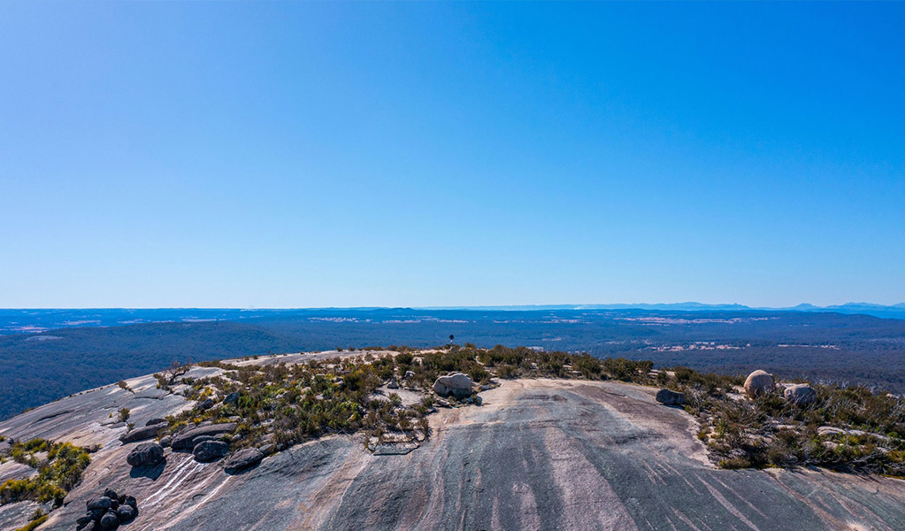 A large smooth, striped rock at Bald Rock with scenic views of New South Wales and Queensland Credit in the distance. Credit: Joshua J Smith &copy; DCCEEW