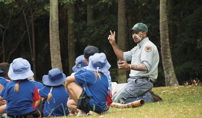 Students sitting on the grass, listening to an Arakwal Aboriginal guide on a school excursion to Walgun Cape Byron State Conservation Area. Photo: David Young/OEH
