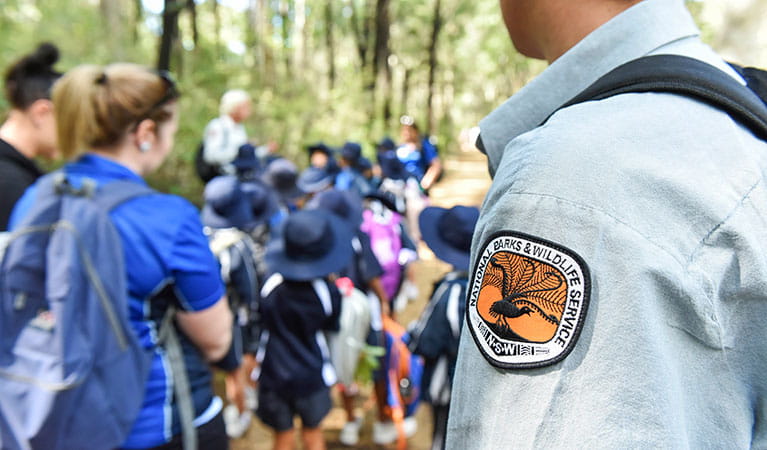 A close up of an NPWS guide's badge with a group of students in the background. Photo: Adam Hollingworth &copy; DPIE