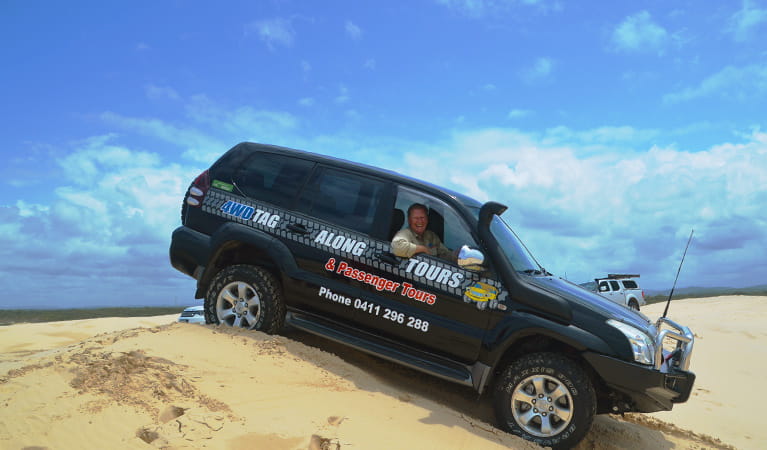 A man in a 4WD vehicle for Tag-Along and Passenger Tours travels down a dune under clear skies. Photo credit: Nicole Boyle &copy; 4WD Tag-Along and Passenger Tours