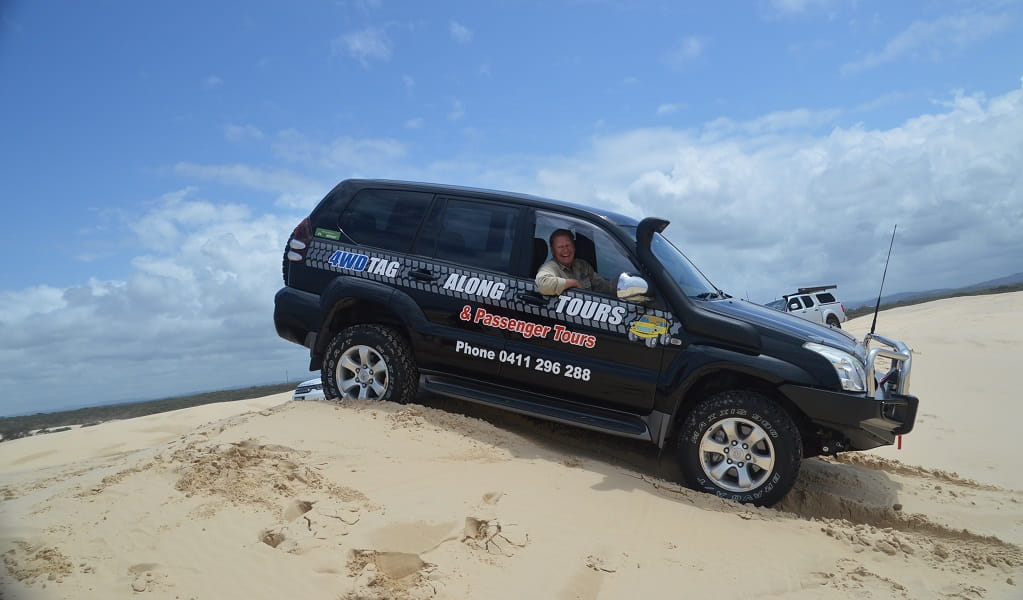 A man in a 4WD vehicle for Tag-Along and Passenger Tours travels down a dune under clear skies. Photo: Nicole Boyle &copy; 4WD Tag-Along and Passenger Tours