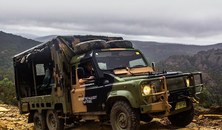 Open-back 4WD vehicle with camouflage paint on a rugged landscape overlooking valleys and mountains. Photo &copy; Beyond the Blacktop 4WD Tours