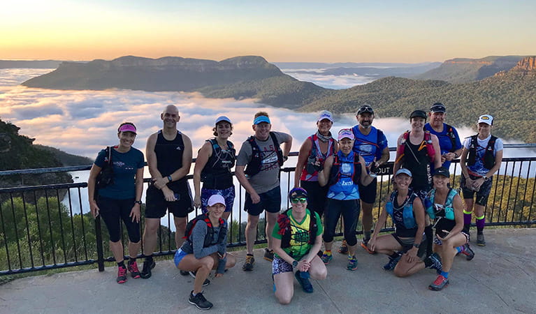A group of runners stand on a lookout platform in front of a sweeping view of mountains and mist-filled valleys. Photo credit: Tony Williams &copy; Blue Mountains Fitness