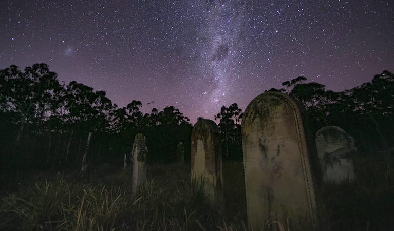View of a dramatic and starry night sky  over an historic graveyard with tombstones, set in bushland. Photo credit: Pete Clifford &copy; Blue Mountains Mystery Tours