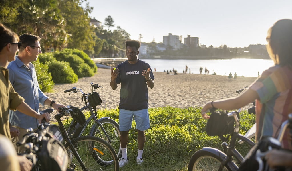 A group of cyclists taking a break by the beach with their friendly Bonza Bike Tours guide. Credit &copy; Destination NSW