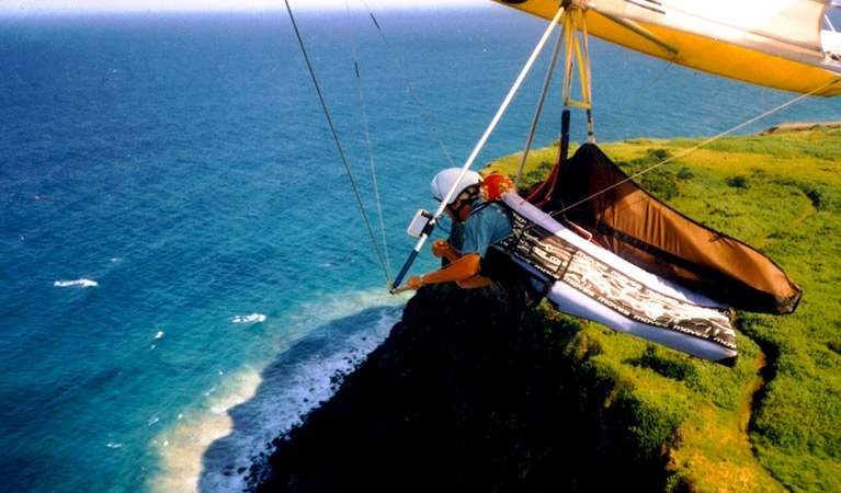 A hang glide instructor flies tandem with a student over dramatic cliffs toward the open ocean. Photo credit: Brian Rushton &copy; Byron Airwaves Hang Gliding School