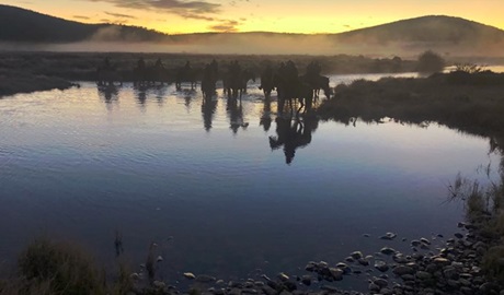 Twilight mountain landscape with river foreground and silhouetted riders on horseback. Photo &copy; Cochran Horse Treks