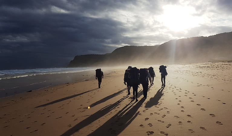 Bushwalkers with backpacks walk along a pristine beach at sunrise in the Royal National Park.  Photo credit: Mark Coulter &copy; Collaroy Centre