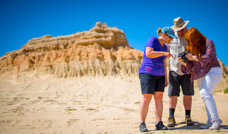 A group of 3 people gather near a Walls of China  rock formation in Mungo National Park. Photo credit: Robert Klarich &copy; Discover Mildura