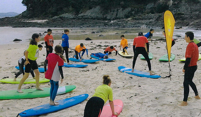 A group of surfers with boards practice stance alongside their instructor at a beach. Image &copy; Gary Hughes Surface School of Surf