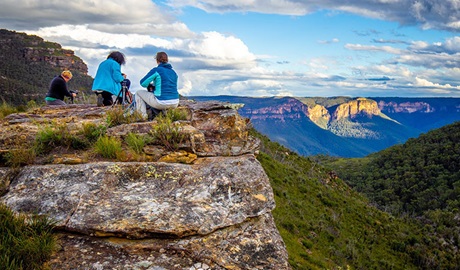 3 people with camera equipment on a rock ledge overlooking a steep valley with sweeping mountains views. Photo &copy; Gary P Hayes Photography