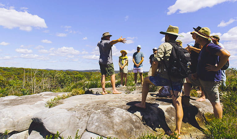 A Girra Girra guide standing on a weathered rock platform shares his knowledge with a group of tour guests. Photo &copy; Girri Girra Aboriginal Experiences