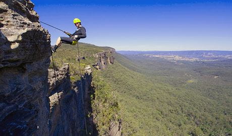 A man abseils down cliff face in the Blue Mountains against a backdrop of valleys and hills. Photo &copy; Neil Aldred 