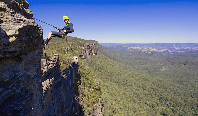 A man abseils down cliff face in the Blue Mountains against a backdrop of valleys and hills. Photo &copy; Neil Aldred 